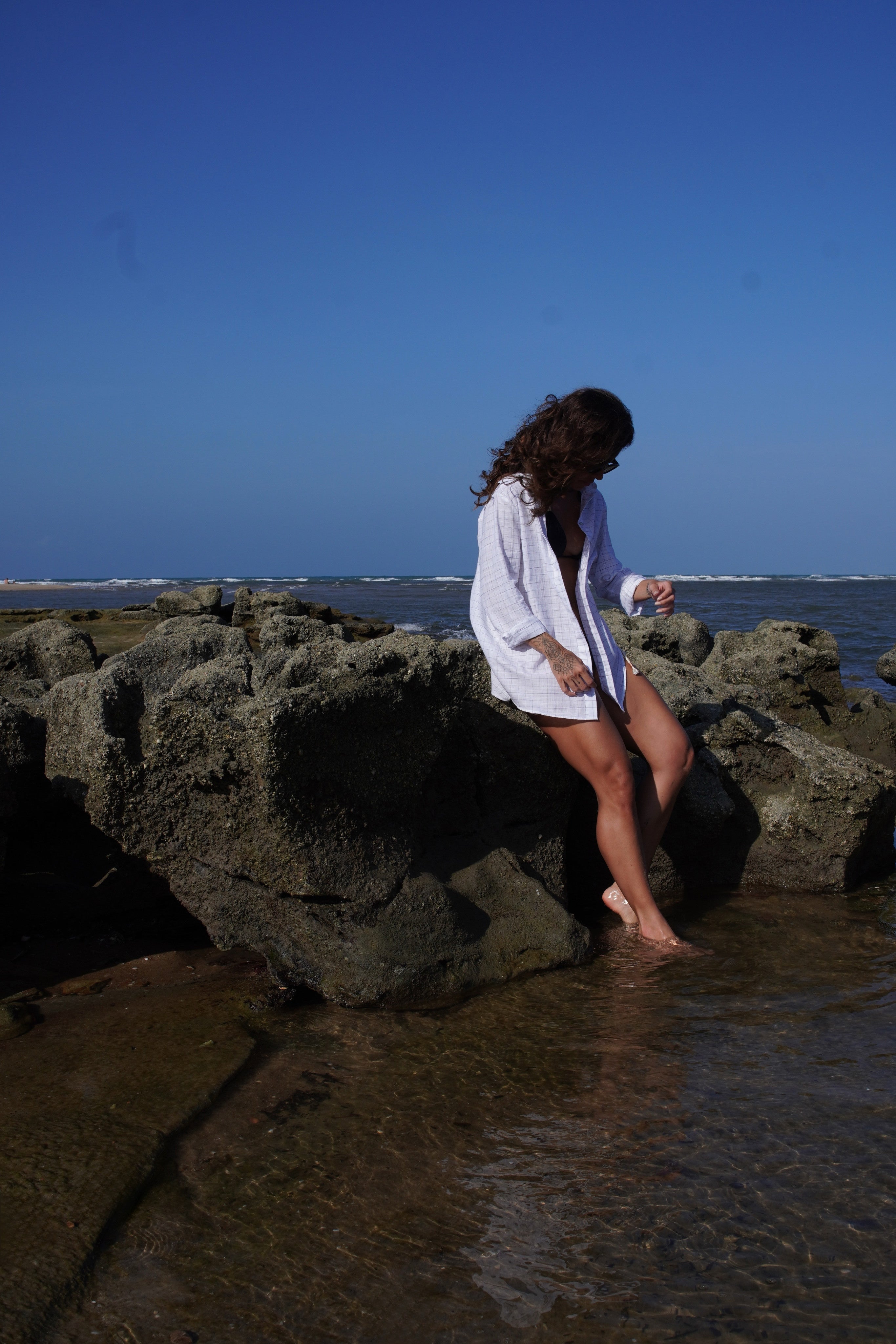 Woman standing on rocks by the ocean with a clear blue sky