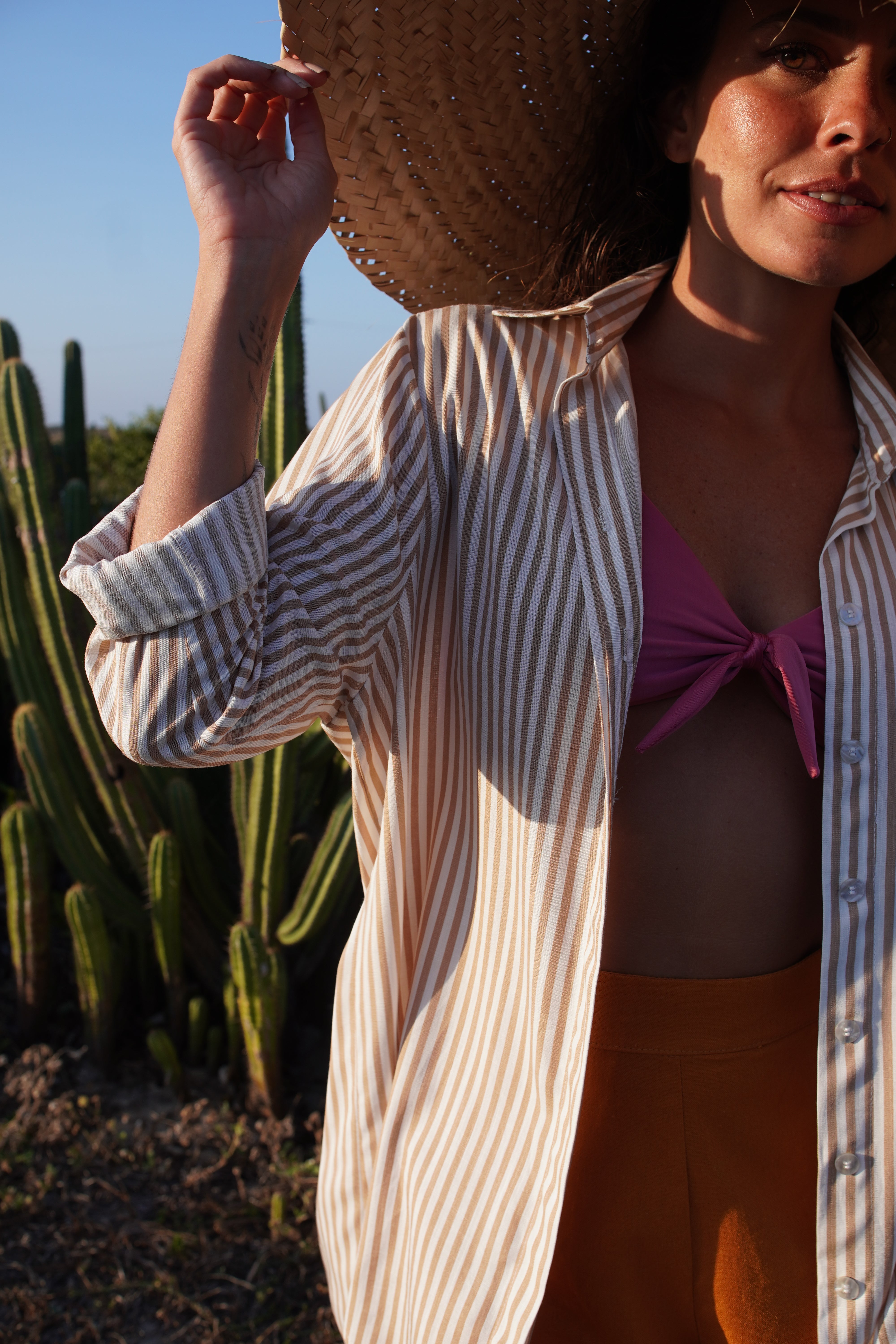 woman wearing a striped shirt and straw hat in a sunlit outdoor setting
