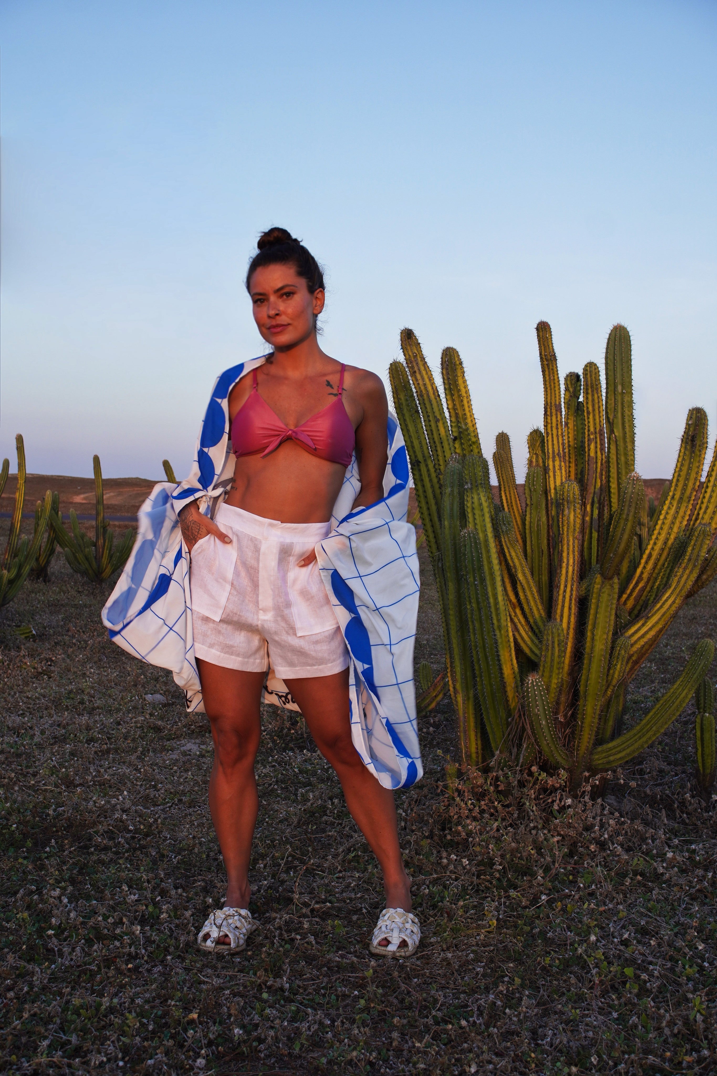 Woman standing in front of a cactus plant with a blue and white pareo draped over her shoulders.
White linen high-rise resort shorts with a relaxed yet tailored silhouette — a timeless warm-weather essential designed for effortless sophistication.