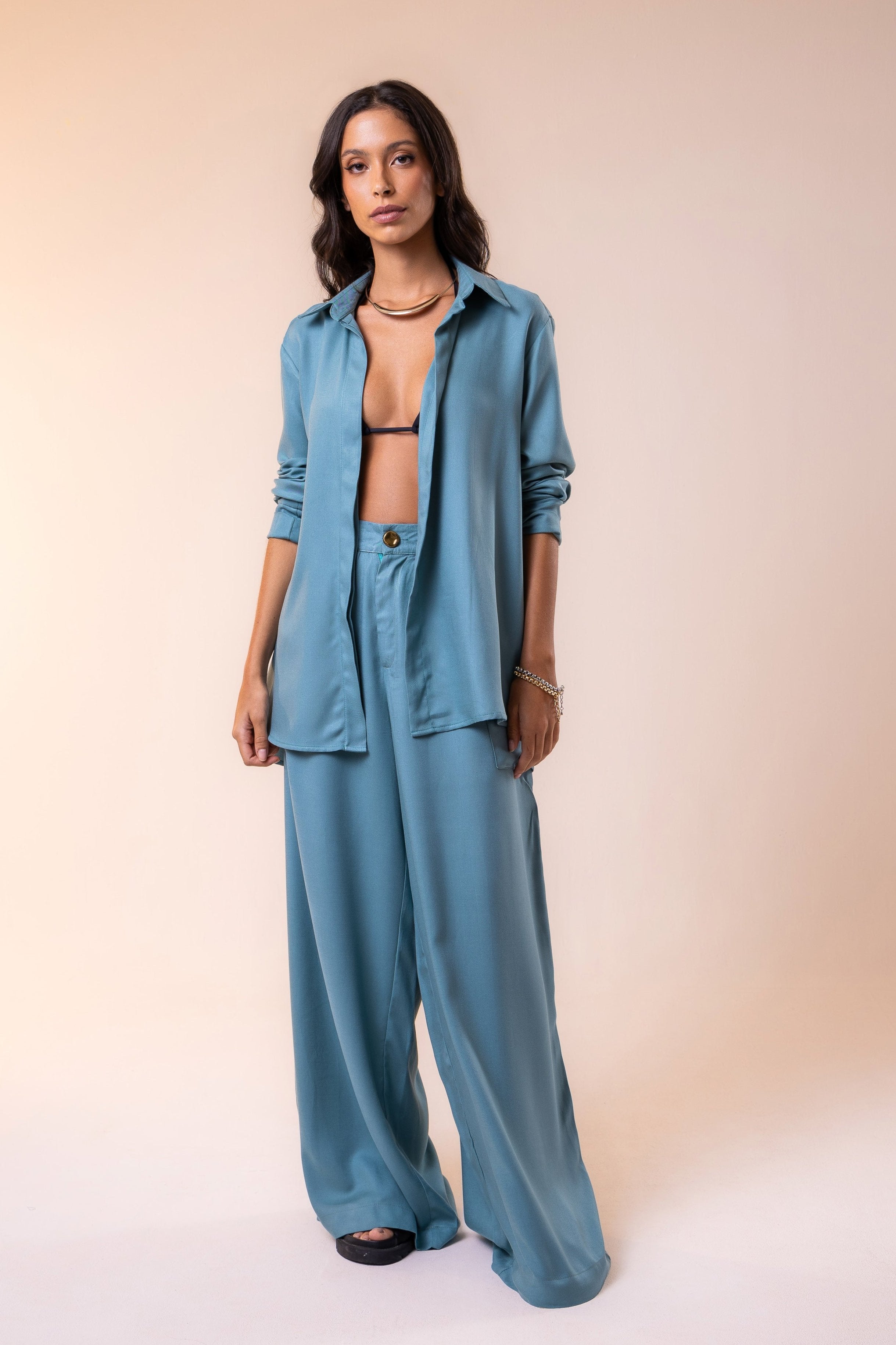 A model wearing a sage green, button-up, long-sleeved shirt with a round neckline, paired with matching wide-leg pants.
Resort co-ord set featuring a lightweight button-down shirt and wide-leg pants in soft blue viscose, blending tropical sophistication with timeless ease
