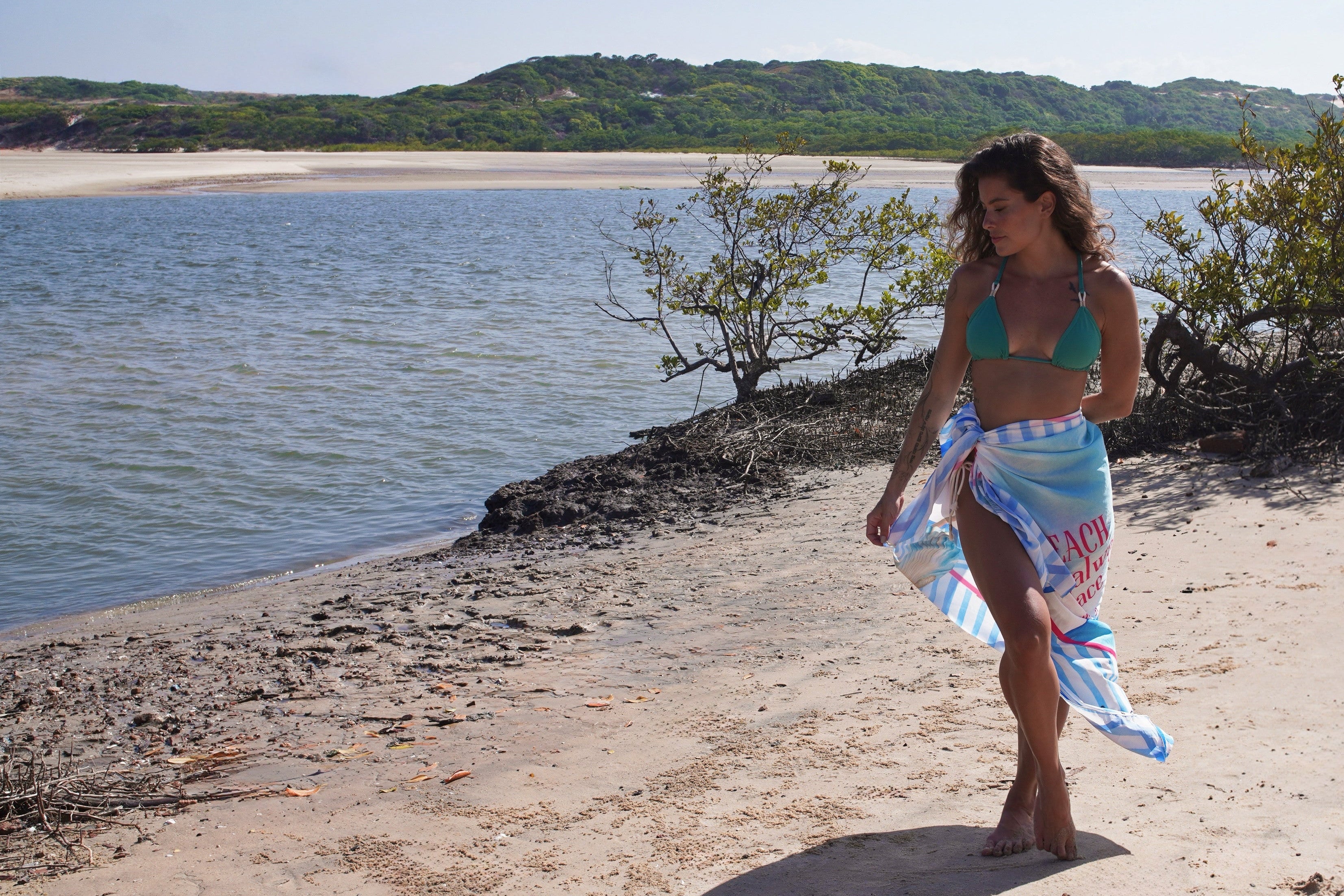 Woman in a green Hoy Swim bikini with handmade detail wears a blue and white printed pareo with pink details by the seaside, embodying the brand’s elegant, tropical, and effortless aesthetic.